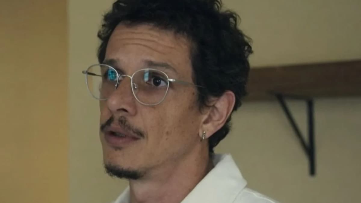 Em cena de Travessia, Gil aparece olhando para a esquerda. Ele usa óculos e está vestindo uma camisa branca.